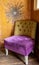 Comfortable chair in corner of living room, upholstered in purple and mustard colour velvet fabrics.