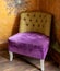 Comfortable chair in corner of living room, upholstered in purple and mustard colour velvet fabrics.