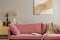 Comfortable velvet pastel pink couch in elegant beige interior with abstract painting