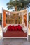 Comfortable wooden alcove couch with striped soft mattress, red pillows and orange curtains. Modern sofa.