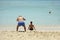 Comic and funny situation. An elderly man takes photos of back view of beautiful girl sitting on the beach