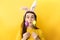 Comic young woman wears bunny ears makes funny face, plays fool, holds colored eggs, has happy expression, dressed in sweater