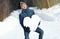 Comical man with great difficulty holding huge heavy heart made of snow, in winter park. Declarations of love, romantic feelings