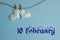 Commemorative date of February 10 on a blue background with white hearts with clothespins, flat lay. Holiday calendar concept,