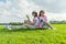 Communication of parent and teenager. Mother and teen daughter sitting on green lawn in the park and reading book, drinking cool c