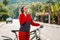 Communication. A young beautiful smiling woman is making a phone call and pushing a Bicycle. Sunny street on the background.