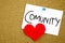 Community word with red heart on a sticky note against a cork notice