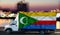 Comores flag on the side of a white van against the backdrop of a blurred city and river. Logistics concept