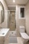 Compact bathroom with bright lighting from ceiling. Beige granite tiles on walls. White toilet bowl and sink on dressing