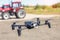 Compact black drone quadcopter with surveillance camera flying low against red agricultural tractor machines. Usage modern