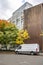 Compact cargo mini van delivered goods to client at multi-apartment high-rise building with wood wall and standing on the autumn