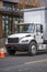 Compact day cab white big rig semi truck with box trailer standing on the city street with multilevel apartments building