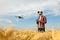 Compact drone hovers in front of farmer with remote controller in his hands. Quadcopter flies near pilot. Agronomist