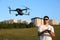 Compact drone hovers in front of man with remote controller in his hands. Quadcopter flies near pilot. Guy taking aerial