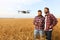 Compact drone hovers in front of two hipster men. Quadcopter flies near farmer and agronomist exploring harvest with