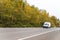 Compact mini van with leaders on the roof driving on autumn road with yellow trees