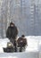 Compact snowmobile for hunting - motorcycle towing pulls two hunters at sunny winter countryside