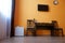 Compact white refrigerator, a table, two chairs, an electric kettle and a wall-mounted TV in the interior of a small studio