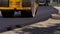Compactor is driving over freshly poured asphalt and compresses it on the road to fix a hole. Close-up of road roller