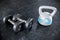 Comparing a pair of dumbbells with a plastic kettlebell. Both lying on the rubber matting of a gym or fitness center.