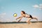 Competitive young woman athlete playing beach volleyball, hitting ball with hands and falling down on sand. Match