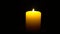 In complete darkness, a large yellow holiday candle is lit with a burning match. The hand is in the frame.