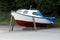 Completely restored small boat taken out of water during winter on local parking lot supported with wooden beams and covered with
