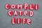 Complicated life, creative red colored stone letters message over green sand