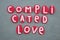 Complicated love, creative text composed with red painted stone letters over green sand