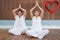 Composite image of attractive couple in white sitting in lotus pose with hands together