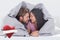 Composite image of attractive couple wrapped in the duvet