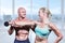 Composite image of cheerful trainer helping woman for lifting dumbbell