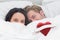 Composite image of couple hiding under the duvet