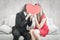 A Composite image of cute geeky couple kissing and holding heart over faces