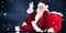 Composite image of santa sits leaned on his bag and waves