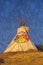 Composite image of a teepee silhouetted at dusk and Indian petroglyphs in the sky