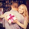 Composite image of woman holding present while hugging boyfriend