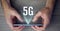 Composition of 5g text over man\'s hands holding smartphone with multiple light trails