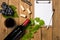 Composition with bottle and glass of wine with grape bunch and vine leaves and notepad on wooden background. Top view with copy