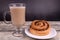 A composition of a cup of cappuccino and a bun on dark and wooden background
