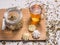 Composition with dried chamomile, glass mug with hot tea, meringues, bamboo board and dried herbal leaves and petals