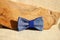 Composition: Extravagant blue bow tie and wooden stick curve on a beige background.