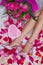 Composition, female feet in sandals on a sheet with rose petals, and a bouquet of roses and a box in the form of a heart with a gi