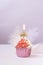 Composition with festive cupcakes with pink cream and a candle on a pink background.