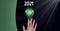 Composition of green copy space over year 2021, hand and lit green lightbulb, on black