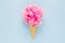 Composition of ice cream cone with pink wisp of bast on a light blue background