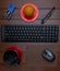 Composition of keyboard, mouse on pad, stapler, eyeglasses, an orange and a cup with drink inside, on wooden table