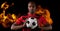 Composition of male football player holding ball over flames on black background