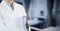 Composition of midsection of male doctor in lab coat with clipboard over out of focus hospital