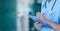 Composition of midsection of male surgeon in scrubs writing on clipboard over out of focus hospital